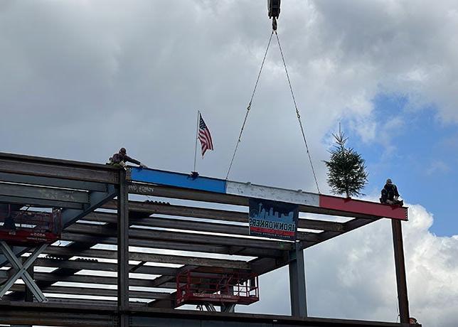 2个人在顶部的钢结构两侧各搭一个红色, 白色和蓝色的横梁上有一面美国国旗和一棵常青树